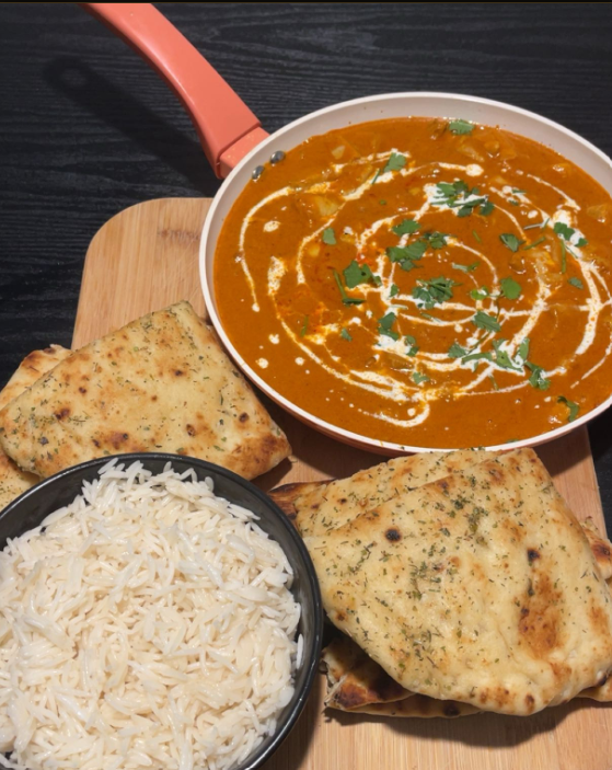 Creamy curry served with rice and naan on a white bowl and wooden board